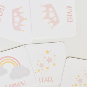 May include: A set of pink and yellow memory game cards featuring images of a crown, stars, and a rainbow. The cards are labeled with the words "crown", "stars", and "rainbow". The cards are part of a memory game by Goodnight Fox.