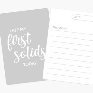 May include: A gray card with the text "I ate my first solids today" in white. A white card with lines for writing a date and a story is attached to the gray card.