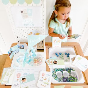 May include: A wooden playset with a travel agency theme. The playset includes a cash register, a booking form, a passport station, and a luggage station. The playset is decorated with travel-themed images and text, such as "Travel Agency", "Booking Form", "Passports", and "Luggage".