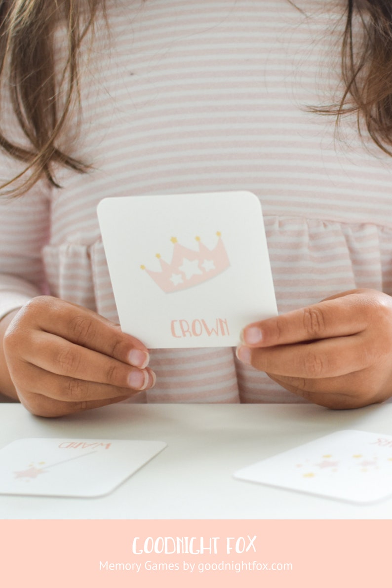 May include: A pink and gold crown card with the word "crown" printed on it. The card is being held by a person's hands. The card is part of a memory game set.