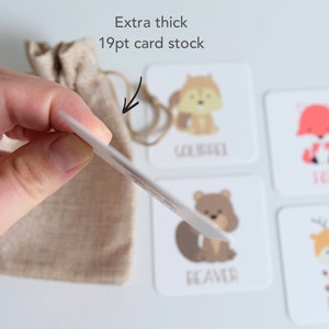 May include: A set of four illustrated animal flash cards with the names "Squirrel", "Fox", "Beaver", and "Deer" printed below each animal. The cards are extra thick, 19pt card stock, and are held in a hand with a small burlap bag in the background.