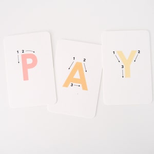 May include: Three white cards with the letters P, A, and Y written in orange, yellow, and pink. Each letter has numbers and arrows indicating the order to trace the letter.