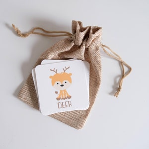 May include: A small burlap bag with a drawstring closure contains a stack of white cards with a cartoon deer illustration and the word "DEER" printed on the front.