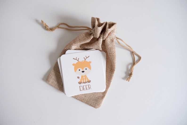 May include: A small burlap bag with a drawstring closure contains a stack of white cards with a cartoon deer illustration and the word "DEER" printed on the front.