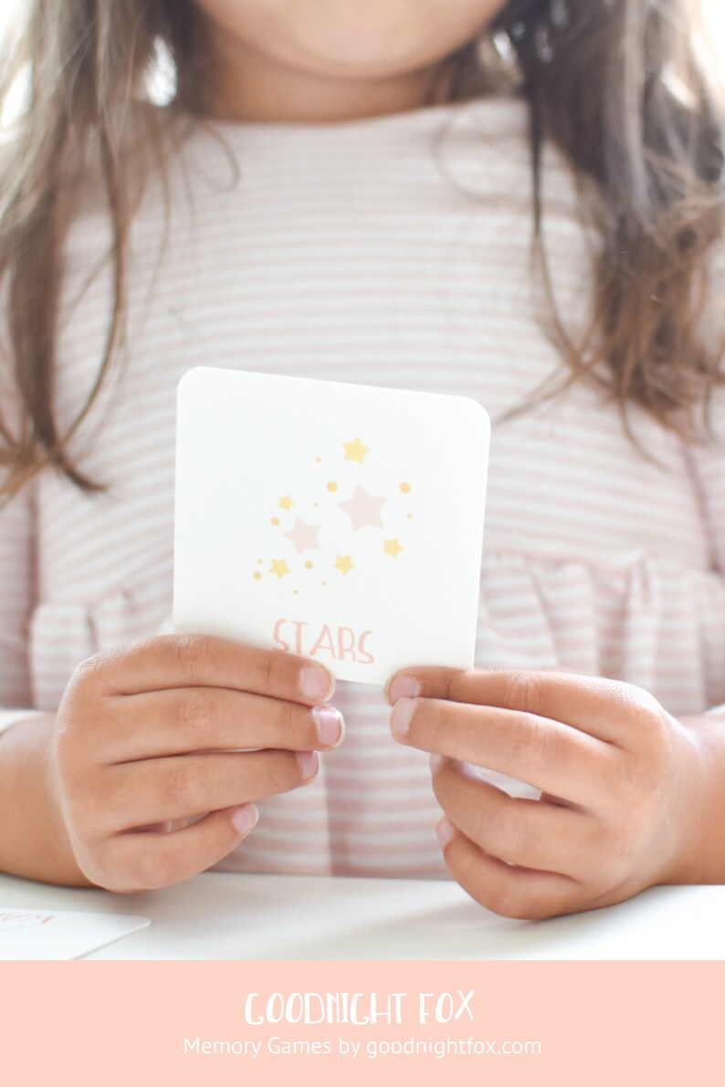 May include: A white card with pink and yellow stars and the word "STARS" printed on it. The card is being held by a child's hands.