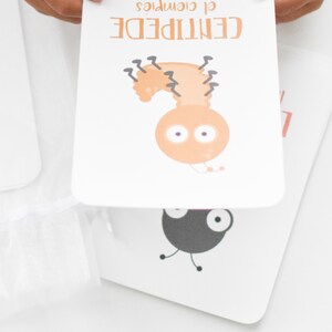 May include: A white card with a cartoon illustration of a brown centipede with black legs and large eyes. The text "CENTIPEDE" is written in black above the illustration and the text "of course" is written in black below the illustration.