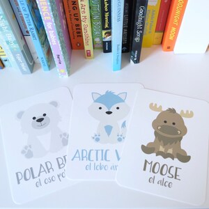 May include: Three illustrated flashcards with images of a polar bear, an arctic wolf, and a moose. Each card has the animal's name in English and Spanish.