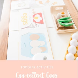 May include: A white wooden play kitchen with a yellow egg carton, a white egg carton, a white card with the word "eggs" on it, a white card with a picture of an egg and a whisk, and a wooden tray with a slice of bread, a green avocado, and a white egg.