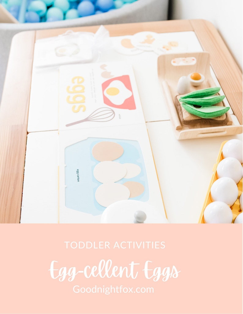 May include: A white wooden play kitchen with a yellow egg carton, a white egg carton, a white card with the word "eggs" on it, a white card with a picture of an egg and a whisk, and a wooden tray with a slice of bread, a green avocado, and a white egg.