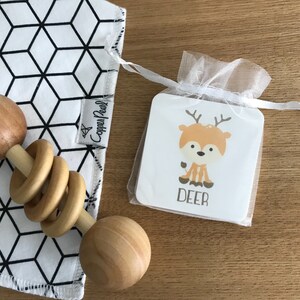 May include: A white and black geometric baby burp cloth with a wooden rattle and a small white card with a cartoon deer and the word "DEER" on it.