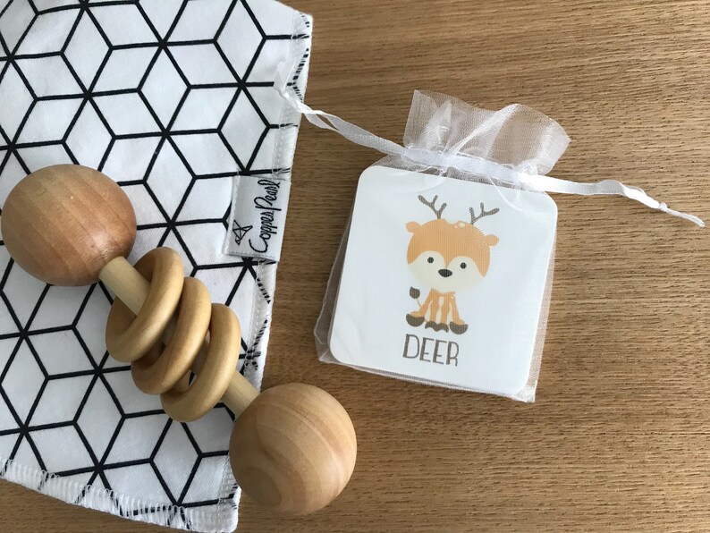 May include: A white and black geometric baby burp cloth with a wooden rattle and a small white card with a cartoon deer and the word "DEER" on it.