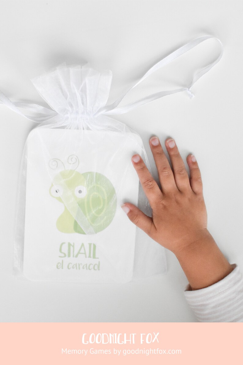 May include: A white organza bag containing a green and white illustrated card. The card depicts a cartoon snail with the words "Snail el caracol" printed on it.