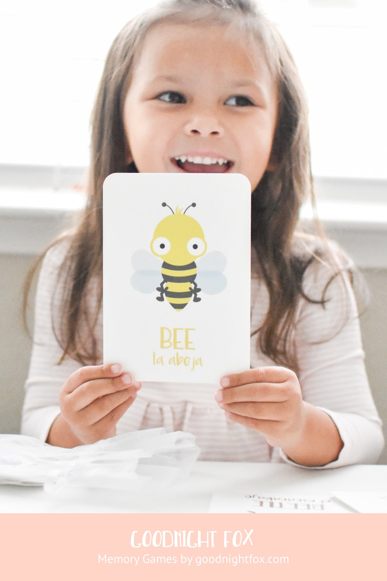 May include: A white card with a cartoon bee illustration and the words "BEE la abeja" in yellow text. A young girl is holding the card in front of her.