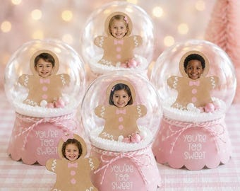 Könnte beinhalten: Vier durchsichtige Kunststoff-Schneekugeln mit rosafarbenen, gewellten Sockeln und der Aufschrift 'YOU'RE TOO SWEET'. In jeder Kugel befindet sich ein brauner Lebkuchen-Ausschnitt mit Kindergesicht und rosa Akzenten.