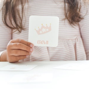 May include: A pink and white card with a gold crown and the word "crown" printed on it. The card is being held by a child.