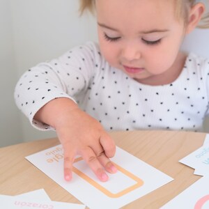 K&ouml;nnte beinhalten: Ein Kind zeigt auf eine wei&szlig;e Karte mit einem goldenen Rechteck und den W&ouml;rtern "agile" und "auto" darauf. Die Karte ist Teil eines Kartensets mit verschiedenen Formen und W&ouml;rtern.