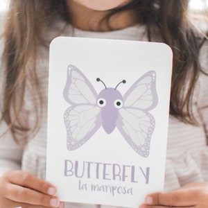 May include: A purple butterfly with large eyes on a white flashcard. The card also includes the word "BUTTERFLY" and the Spanish translation "la mariposa".