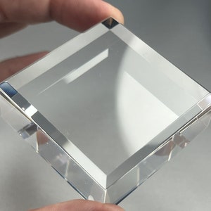 Puede incluir: Un pisapapeles cuadrado de vidrio transparente con bordes biselados.