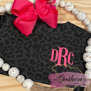 May include: Black and gray leopard print t-shirt with a pink monogram "DRC" and the text "Young Southern Mess" in pink.