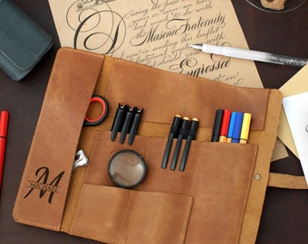 May include: A brown leather roll-up case with multiple pockets for pens, pencils, and other writing tools. The case has a personalized inscription that reads "M Michael".