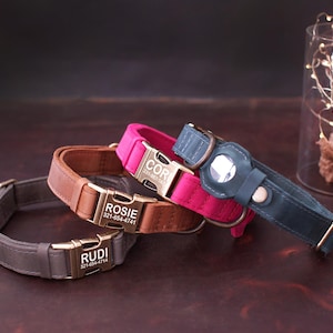 May include: Three personalized dog collars in gray, brown, and pink. Each collar has a metal buckle with a name and phone number engraved. The blue collar has a circular attachment. The collars are on a dark brown surface.