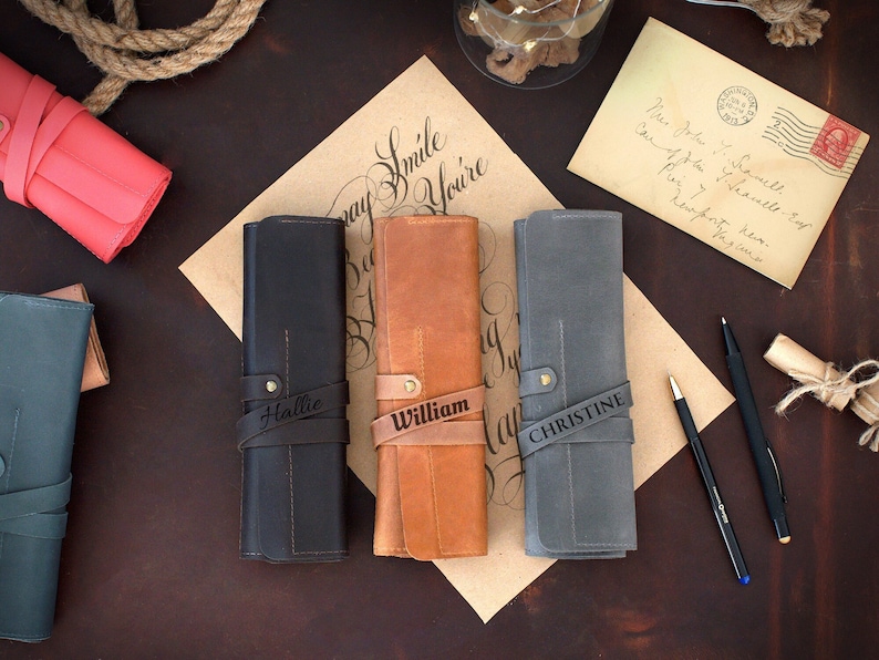 May include: Three personalized leather pencil cases in black, brown, and gray with the names Hallie, William, and Christine engraved on them.