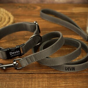 May include: A gray dog collar and leash set. The collar has a black buckle with the name "Devin" and a phone number. The matching leash also has the name "Devin" engraved. The set is made of a soft, durable material.