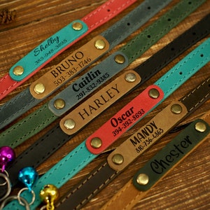 Puede incluir: Un conjunto de ocho collares de perro de cuero personalizados en varios colores, incluidos rojo, azul, verde, marr&oacute;n y negro. Cada collar tiene una hebilla de lat&oacute;n y una campana de metal. Los collares est&aacute;n grabados con nombres y n&uacute;meros de tel&eacute;fono.