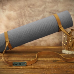 May include: A gray yoga mat with a brown leather strap and the name "ALICE" embossed on the strap.