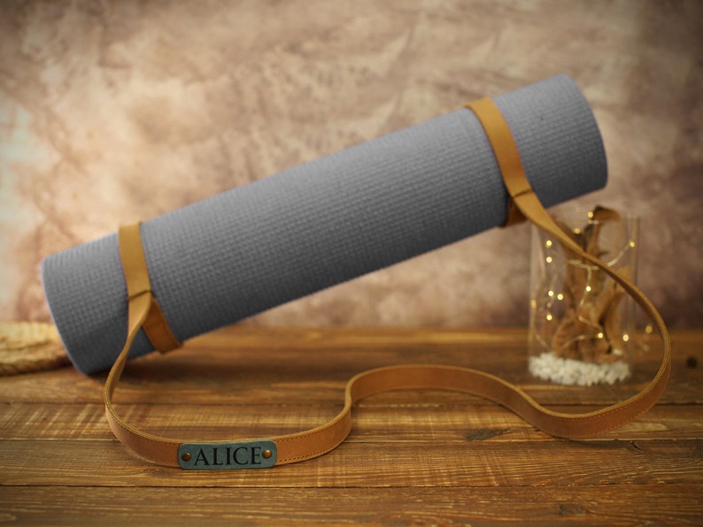 May include: A gray yoga mat with a brown leather strap and the name "ALICE" embossed on the strap.