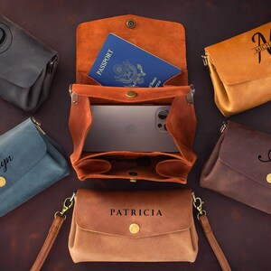 May include: A collection of leather crossbody bags in various colors, including brown, tan, blue, and gray. One bag is open, revealing a passport and a smartphone. Each bag features a personalized initial or name.