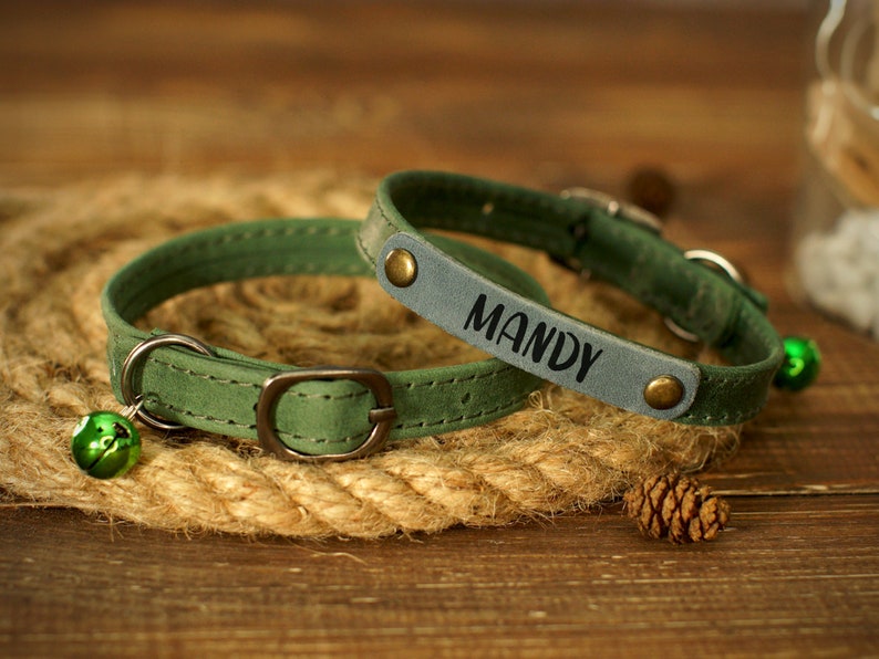 Puede incluir: Dos collares de perro de cuero verde con hebillas plateadas y cascabeles. El collar m&aacute;s grande tiene el nombre "Mandy" grabado en &eacute;l.