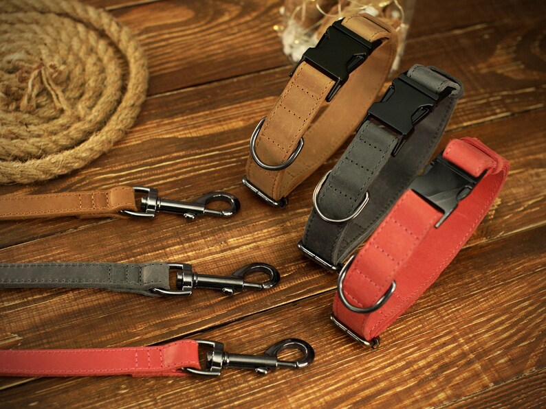 May include: A selection of dog collars and leashes in various colors, including tan, gray, and red. The collars feature black buckles and metal D-rings. The leashes have matching colors and metal clasps. The items are arranged on a wooden surface.