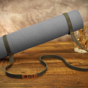 May include: A gray yoga mat with a brown leather strap and a personalized name tag that reads "EVA".