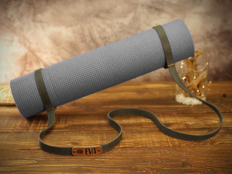 May include: A gray yoga mat with a brown leather strap and a personalized name tag that reads "EVA".