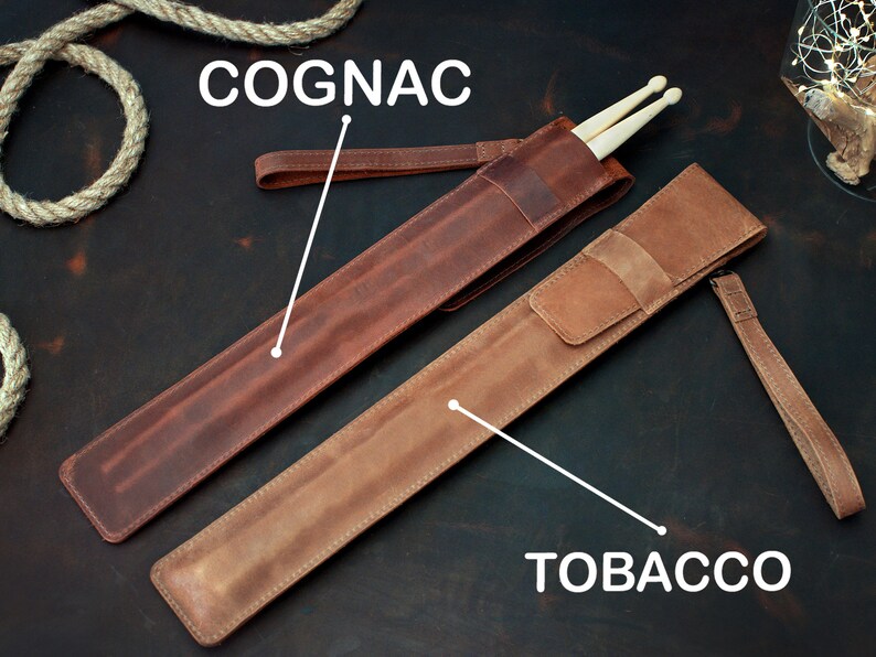 Op de afbeelding: Twee leren drumstick-hoezen, een in cognac en een in tabak. Beide hoezen hebben een band.