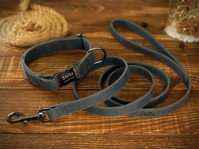 May include: A gray dog collar and matching leash set. The collar has a metal buckle with the name "Stella" and a phone number. The leash also has the name "Stella" printed on it. The set is made of a soft, durable material.