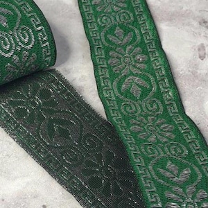 May include: A roll of green and silver decorative ribbon with a floral and geometric pattern. The ribbon is a deep forest green with a metallic silver design. The ribbon is likely used for crafts, sewing, or embellishments.