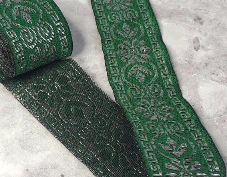 May include: A roll of green and silver decorative ribbon with a floral and geometric pattern. The ribbon is a deep forest green with a metallic silver design. The ribbon is likely used for crafts, sewing, or embellishments.