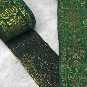 May include: A roll of green and gold decorative ribbon with a floral pattern. The ribbon is made of a woven material and has a metallic sheen. The ribbon is unrolled, revealing the intricate design.