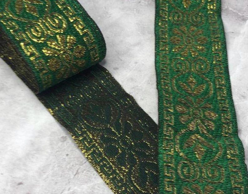 May include: A roll of green and gold decorative ribbon with a floral pattern. The ribbon is made of a woven material and has a metallic sheen. The ribbon is unrolled, revealing the intricate design.