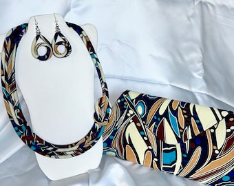 May include: A set of matching jewelry and a clutch bag. The necklace, earrings, and clutch are all made of fabric with a brown, blue, and white abstract pattern.