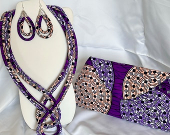 May include: A purple and white patterned fabric necklace, matching earrings, and a clutch purse. The necklace is a long, multi-strand design with a knot at the bottom. The earrings are teardrop shaped. The clutch is a rectangular shape with a flap closure.