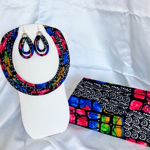 May include: A colorful fabric necklace and matching earrings with silver accents. A matching fabric clutch with a black, white, blue, green, and pink geometric pattern.