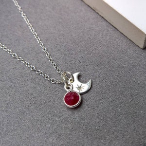 May include: A silver chain necklace with a red gemstone pendant and a silver crescent moon charm with a star.