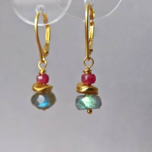 May include: Gold dangle earrings with a layered design featuring a teardrop-shaped labradorite gemstone, a gold disc, and a pink gemstone.