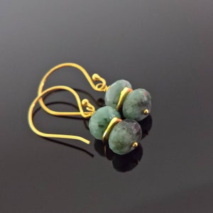 Puede incluir: Un par de pendientes de oro con cuentas de piedras preciosas verdes. Los pendientes tienen un diseño sencillo con un pequeño bucle de oro en la parte superior.
