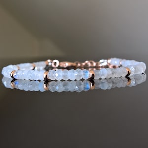 Puede incluir: Un delicado brazalete hecho con cuentas de piedra lunar blanca y detalles en oro rosa. El brazalete está enhebrado en una cadena de plata.