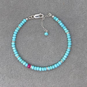 May include: A turquoise and silver beaded bracelet with a pink gemstone accent. The bracelet has a silver clasp and extender chain.