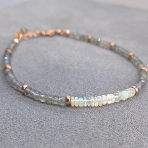 May include: A delicate bracelet made with small, round, grey labradorite and white opal beads. The bracelet has a rose gold clasp.